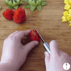 a person cutting strawberries with scissors on a wooden table next to cut up fruit