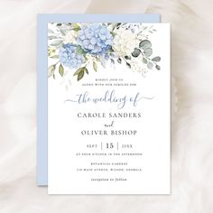 a wedding card with blue flowers and greenery on the front, is displayed against a white background