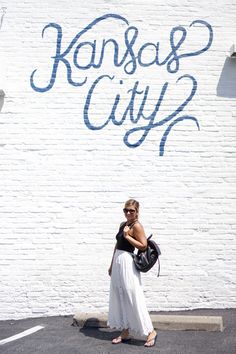 a woman standing in front of a white brick wall with the words kansas city painted on it