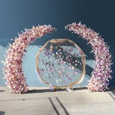 an arch made out of pink flowers is shown in front of a blue wall with a mirror