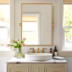 a white sink sitting under a mirror next to a vase with pink flowers in it