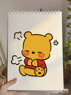 a hand holding a notebook with a drawing of a teddy bear on it