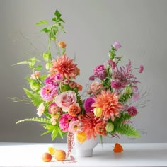 a white vase filled with lots of colorful flowers on top of a table next to fruit