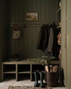 a well - lit mud room with green walls and wood paneling, two coats hanging on the wall