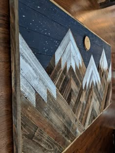 a wooden wall hanging on the side of a building with mountains painted on it's sides