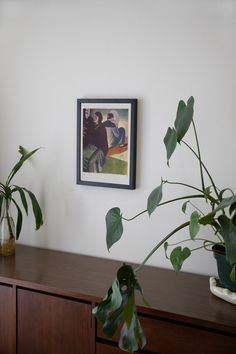 two potted plants sit on top of a wooden dresser next to a framed painting