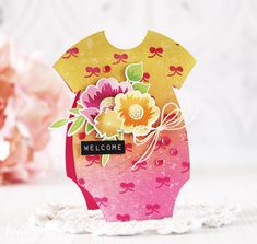 a pink and yellow welcome card with flowers in the front on a doily table