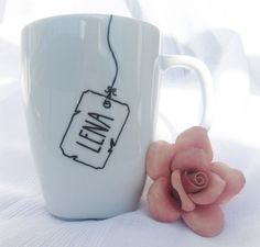 a white coffee cup with a tag on it next to a pink flower and the words individualiser bar