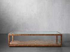 a glass and wood coffee table against a gray wall with concrete flooring in the background