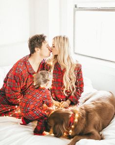 a man and woman in pajamas kissing on a bed with a dog