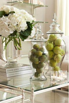 a glass table topped with two vases filled with flowers and fruit next to books