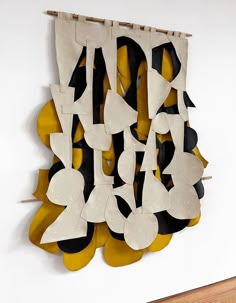 an abstract sculpture made out of paper and wood on a white wall next to a wooden floor