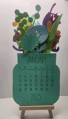 a desk calendar with paper cut out of flowers in the shape of a planter