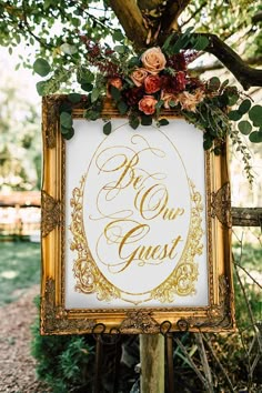 a sign that says, be our guest with flowers and greenery on it in front of a tree