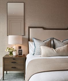 a bedroom with a bed, night stand and mirror on the wall above it's headboard