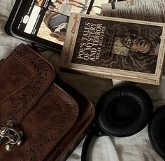 there is a book, headphones, and purse on the bed next to each other