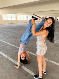 two young women standing in an empty parking lot, one holding the other upside down