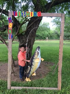 a little boy standing next to a fake fish in front of a sign that says fishing