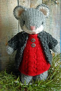 a knitted mouse wearing a red dress and black jacket, sitting on some grass