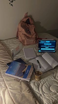 an open laptop computer sitting on top of a bed next to books and other items