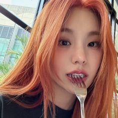 a woman with red hair is holding a fork in her mouth