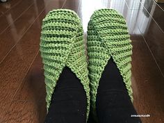 a pair of green slippers sitting on top of a wooden floor next to a person's feet