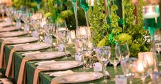 a long table is set with white plates and silverware, green centerpieces and candles