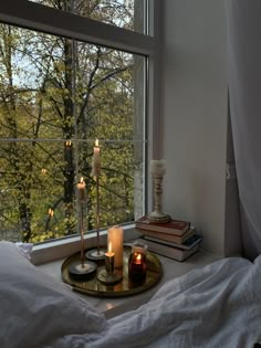 candles are lit on a tray in front of a window with trees out the window