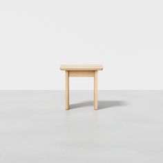 a small wooden table sitting on top of a cement floor next to a white wall