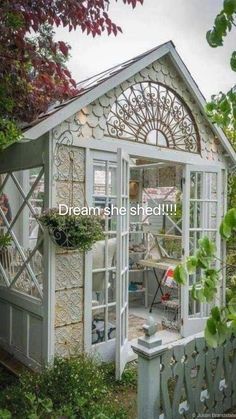 a white garden shed sitting next to a lush green tree