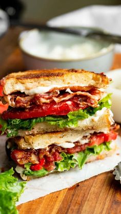 a sandwich with meat, lettuce and tomato on it sitting on a cutting board