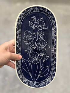 a hand holding up a blue and white plate with flowers on the inside, in front of a gray background