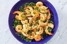 a blue bowl filled with shrimp and greens on top of a marble countertop next to a fork