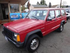 a red jeep is parked in front of a building with other cars and trucks behind it