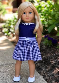 a doll with blonde hair wearing a blue dress and white shoes standing on the sidewalk