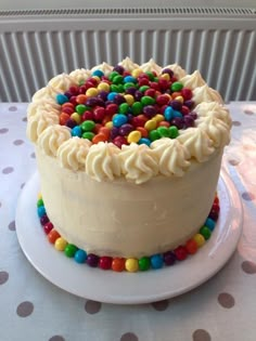 a cake with white frosting and multi colored candy toppings on the top is sitting on a table