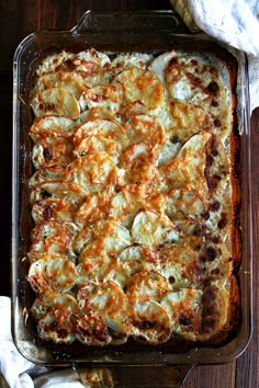 a casserole dish with cheese and vegetables in it sitting on a wooden table