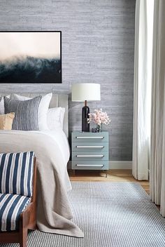 a bed room with a neatly made bed next to a painting on the wall and a dresser