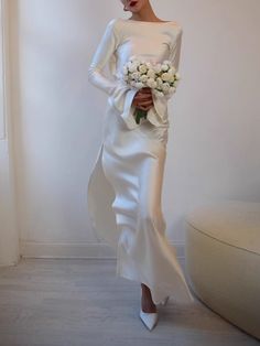 a woman in a white dress holding a bouquet of flowers and standing next to a couch