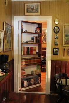 an open book shelf in the corner of a room with pictures on the wall and wooden floors