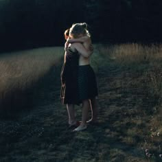 two women hugging each other in the middle of a field