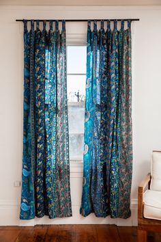 a window with blue curtains and wooden flooring in front of a white chair next to a window