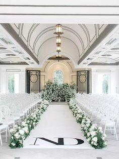 an indoor wedding ceremony with white flowers and greenery on the aisle, along with rows of chairs