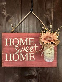 a wooden sign that says home sweet home hanging on a wall next to a mason jar filled with flowers