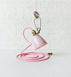 a pink lamp with a cord attached to it and a white brick wall in the background