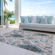 a couch sitting on top of a white floor next to a window covered in blue pillows