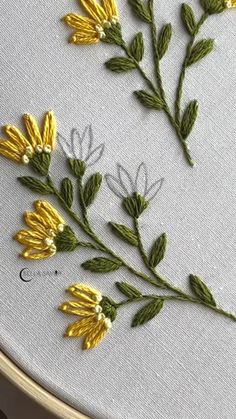 some yellow flowers are sitting on a white table cloth and the embroidery has been stitched onto it