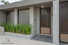 the front entrance to a modern home with plants in pots and shutters on the doors