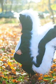 a young child dressed in a skunky costume is standing on the ground with leaves all around