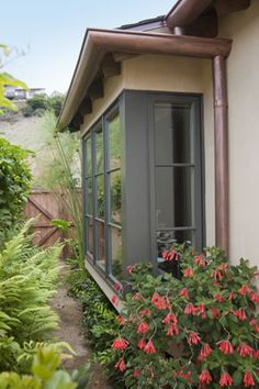 a small house with flowers growing in the front and side windows on either side of it